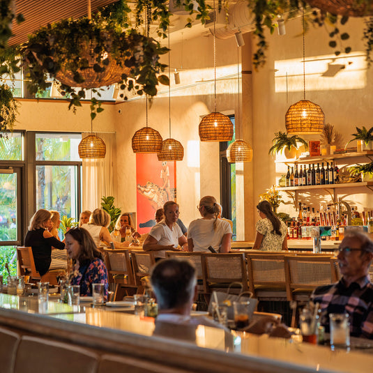 Guests dining and socializing inside the Florida Room bar with warm lighting and tropical decor at The Fort