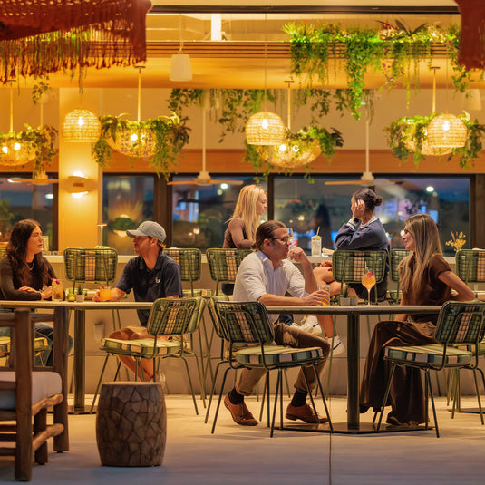 Guests enjoying drinks and conversation at outdoor dining tables in the Florida Room with warm lighting and lush greenery