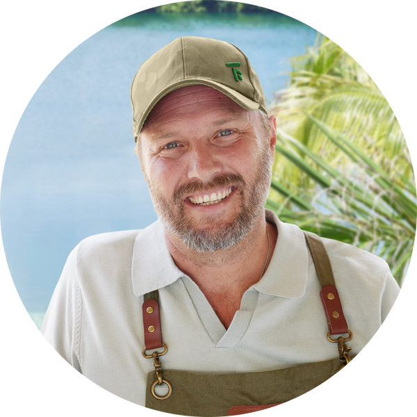 Portrait headshot of Chef Jeff McInnis smiling outdoors with palm trees and water in the background