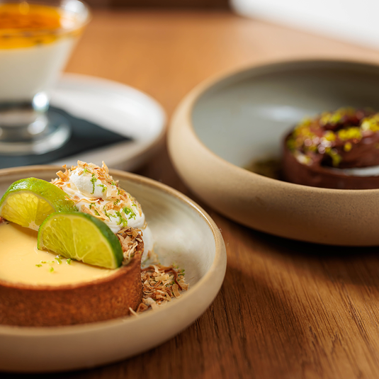 Key lime tart dessert with fresh lime slices, whipped cream, and toasted coconut on a wooden table