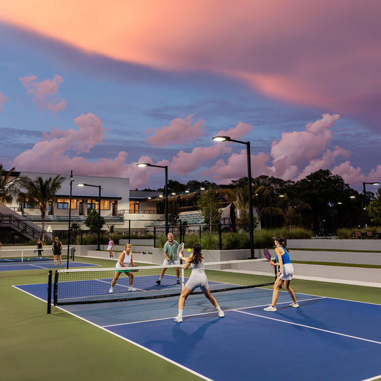 Players enjoying an evening pickleball match at The Fort in Fort Lauderdale with colorful sunset skies over the outdoor courts.